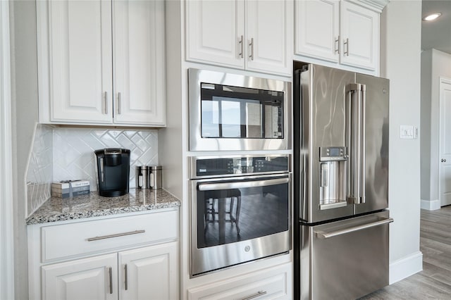 23935 Birchwood Lake Ln, Katy, TX 77493 - kitchen featuring decorative backsplash, baseboards, light stone counters, stainless steel appliances, and light wood-style flooring