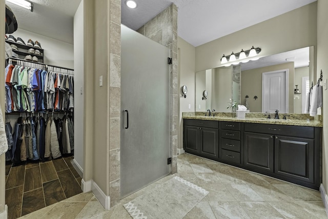 full bath featuring double vanity, baseboards, a spacious closet, a shower stall, and a sink