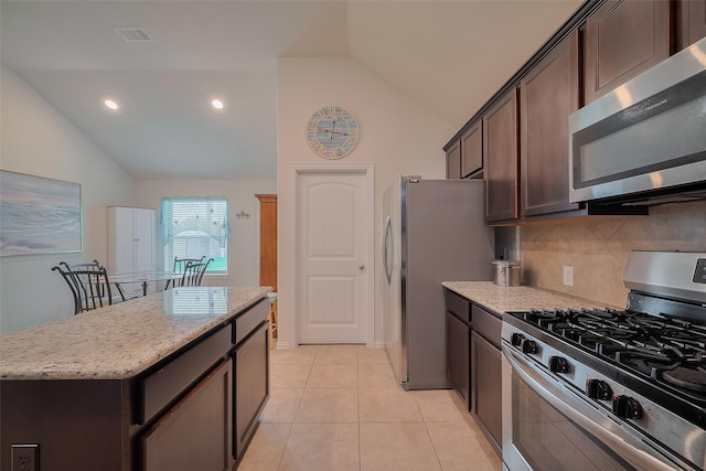 2903 Blue Mist Bnd, Brookshire, TX 77423 - kitchen featuring appliances with stainless steel finishes, lofted ceiling, dark brown cabinets, light stone countertops, and decorative backsplash