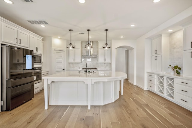 kitchen with visible vents, decorative backsplash, wall chimney range hood, arched walkways, and appliances with stainless steel finishes