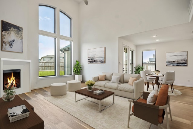 living area featuring light wood-style floors, plenty of natural light, a warm lit fireplace, and a towering ceiling