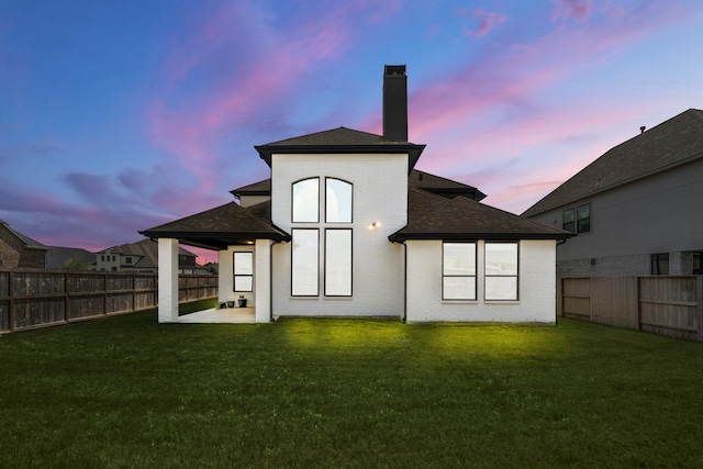 back of property featuring a lawn, a fenced backyard, a chimney, and a shingled roof