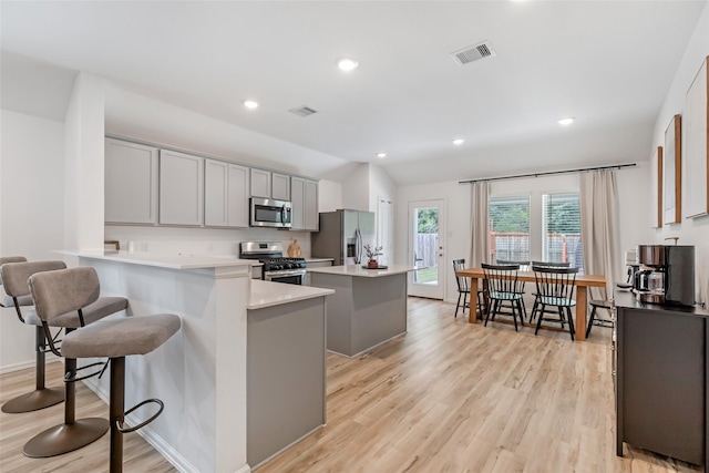 21623 Mount Frisell Ln, Porter, TX 77365 - kitchen with visible vents, appliances with stainless steel finishes, a center island, gray cabinetry, and light wood-style flooring