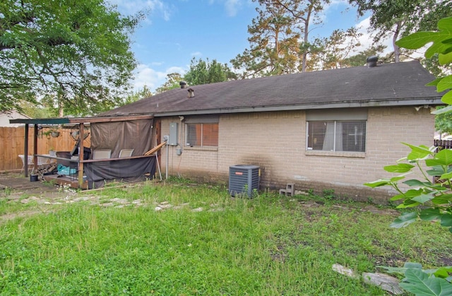 back of house with fence, central AC unit, roof with shingles, and brick siding