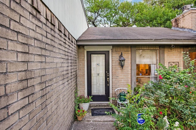doorway to property with brick siding and roof with shingles