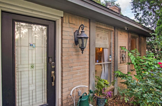 view of exterior entry featuring brick siding and a chimney
