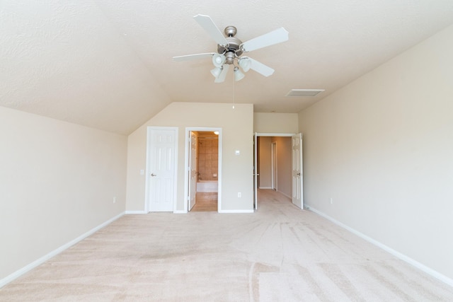unfurnished bedroom with connected bathroom, visible vents, light colored carpet, baseboards, and lofted ceiling
