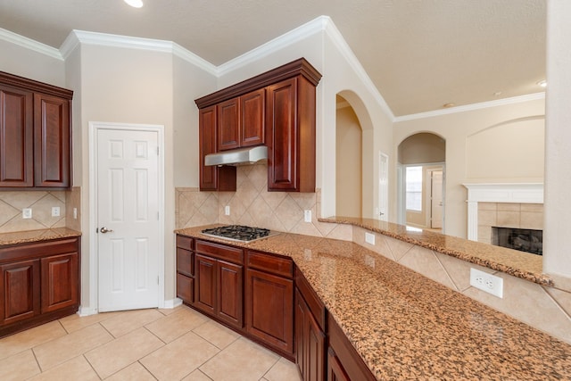kitchen with under cabinet range hood, arched walkways, light stone countertops, and stainless steel gas stovetop
