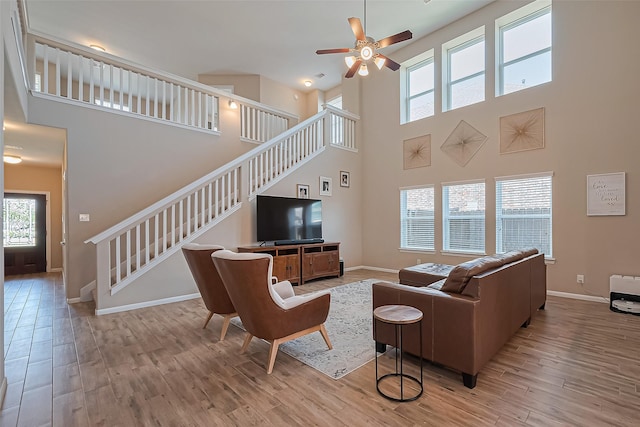 living area featuring stairs, ceiling fan, wood finished floors, and a towering ceiling