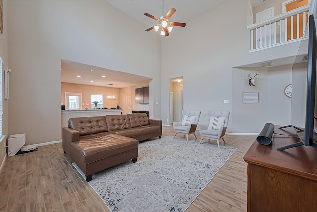 living area featuring a high ceiling, ceiling fan, light wood-style floors, baseboards, and visible vents