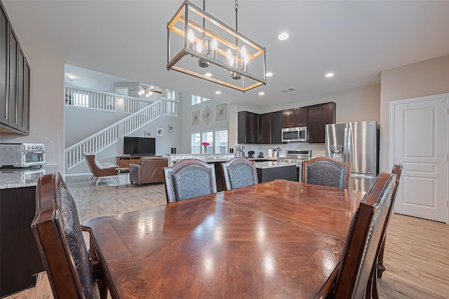 dining area featuring light wood-style flooring, ceiling fan with notable chandelier, a toaster, and stairway