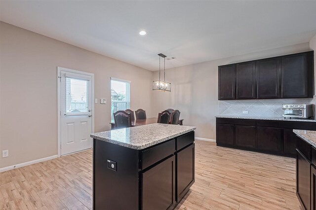 kitchen with a center island, decorative backsplash, light wood finished floors, and decorative light fixtures