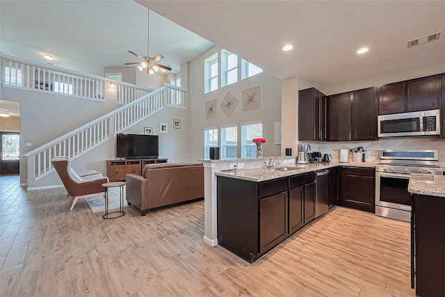 11351 Needlerock Ct, Humble, TX 77396 - kitchen with stainless steel appliances, open floor plan, dark brown cabinetry, light wood-type flooring, and a high ceiling