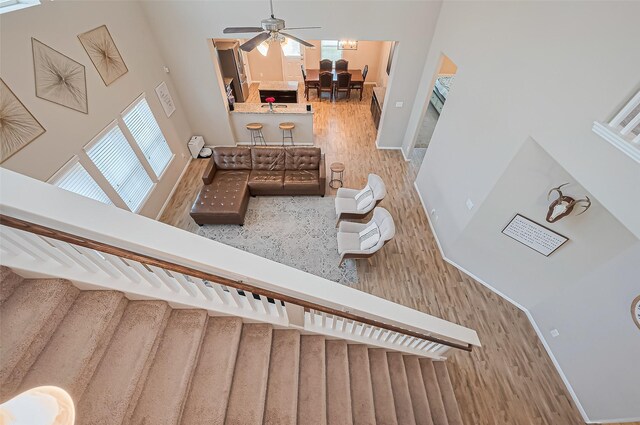 stairway featuring baseboards, ceiling fan, wood finished floors, and a towering ceiling