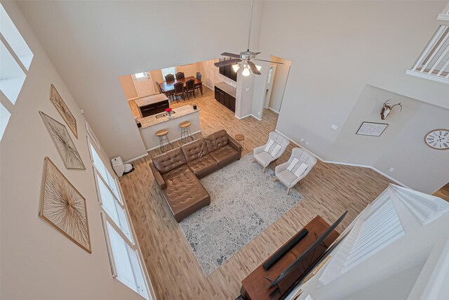 living area with baseboards, a high ceiling, a ceiling fan, and wood finished floors