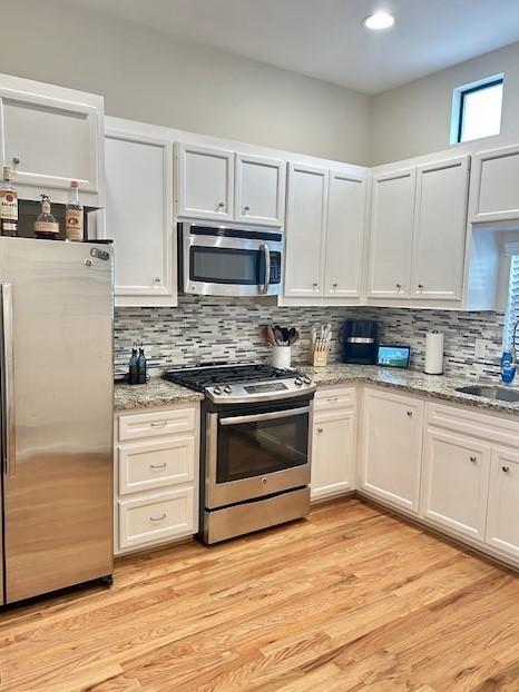 kitchen with appliances with stainless steel finishes, tasteful backsplash, light wood-style flooring, and light stone counters