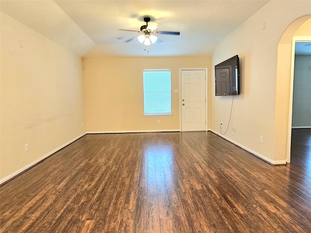 empty room featuring arched walkways, wood finished floors, ceiling fan, and baseboards