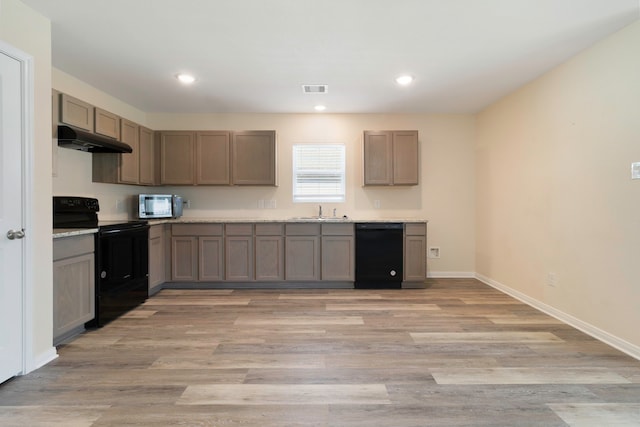 kitchen with a sink, light wood finished floors, under cabinet range hood, visible vents, and black appliances