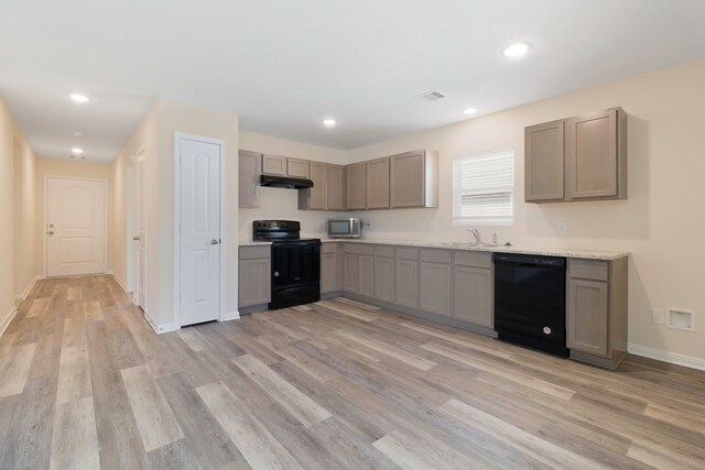 kitchen featuring light countertops, a sink, black appliances, light wood finished floors, and under cabinet range hood