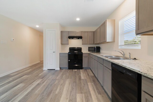 kitchen with a sink, baseboards, black appliances, light wood finished floors, and under cabinet range hood