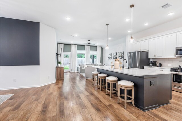 kitchen featuring a kitchen island with sink, open floor plan, white cabinetry, light wood-style flooring, and appliances with stainless steel finishes