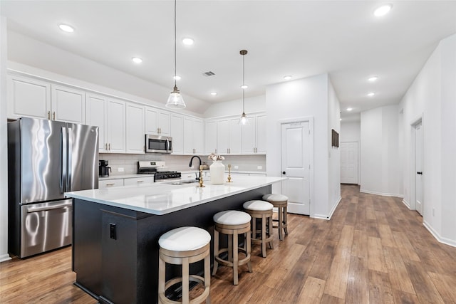 kitchen with appliances with stainless steel finishes, tasteful backsplash, wood finished floors, a sink, and white cabinetry