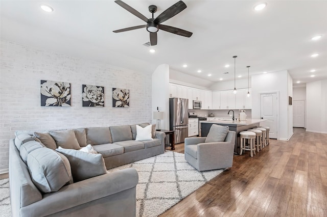 living room with a ceiling fan, brick wall, light wood-type flooring, baseboards, and recessed lighting