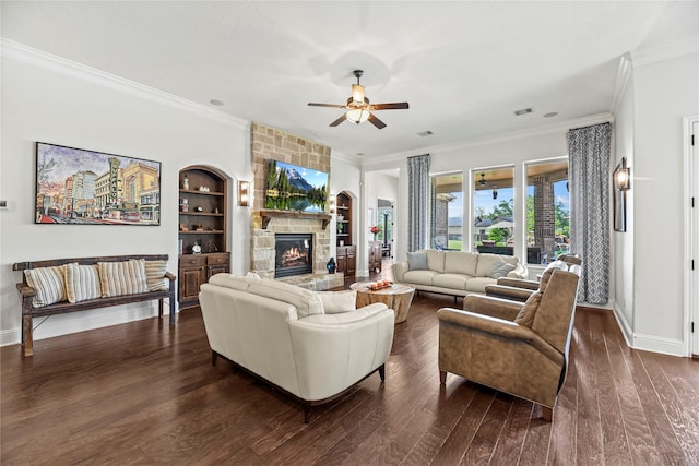 living room with crown molding, dark wood-style flooring, ceiling fan, a stone fireplace, and baseboards