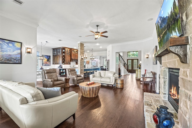 living room featuring crown molding, visible vents, a stone fireplace, and dark wood-type flooring