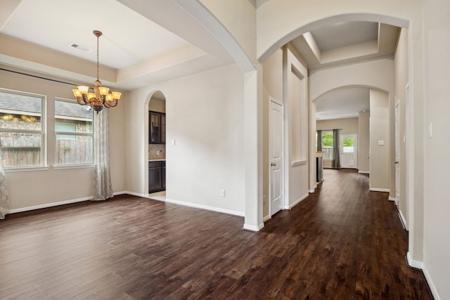 interior space featuring baseboards, a notable chandelier, a raised ceiling, and dark wood-type flooring
