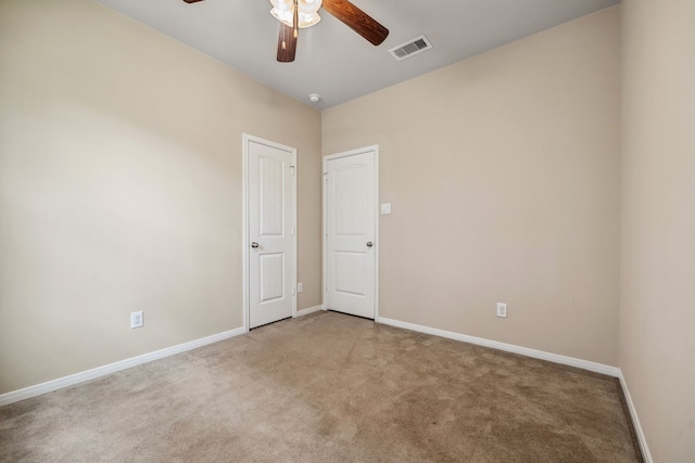 empty room featuring a ceiling fan, light colored carpet, visible vents, and baseboards