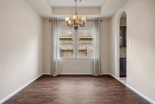 unfurnished dining area with an inviting chandelier, visible vents, a raised ceiling, arched walkways, and dark wood finished floors