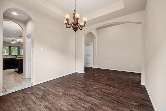 spare room with baseboards, wood finished floors, and ceiling fan with notable chandelier