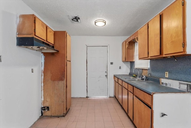 6201 Batterson St, Houston, TX 77026 - kitchen featuring brown cabinetry, a textured ceiling, dark countertops, a sink, and light tile patterned floors