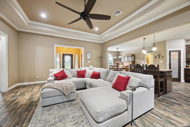 living room featuring a ceiling fan, visible vents, a raised ceiling, dark wood-style floors, and ornamental molding