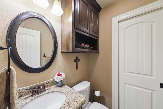 half bath featuring toilet, a textured wall, and a sink