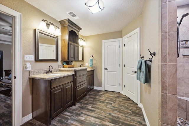 full bath with double vanity, visible vents, wood finished floors, a sink, and baseboards