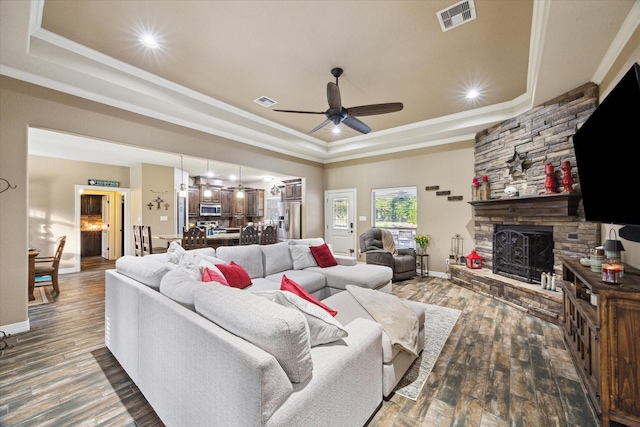 living area with crown molding, a raised ceiling, a stone fireplace, and visible vents