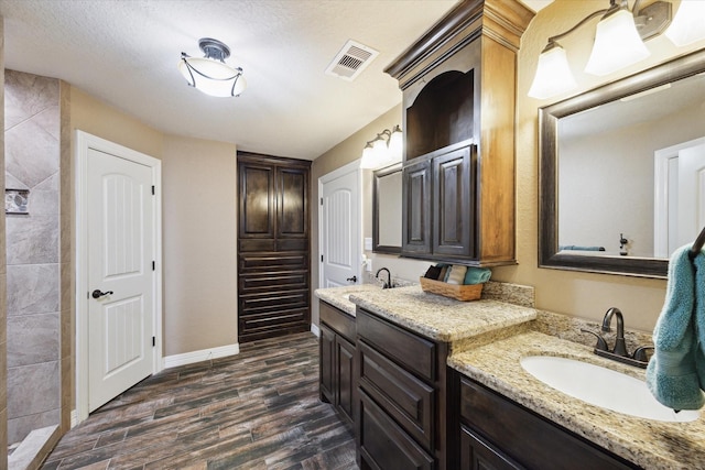 full bath featuring visible vents, wood finished floors, two vanities, a sink, and baseboards