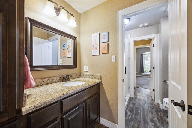 bathroom featuring a textured wall, vanity, toilet, baseboards, and wood finished floors