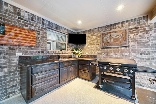 kitchen featuring light carpet, a sink, brick wall, dark stone counters, and recessed lighting