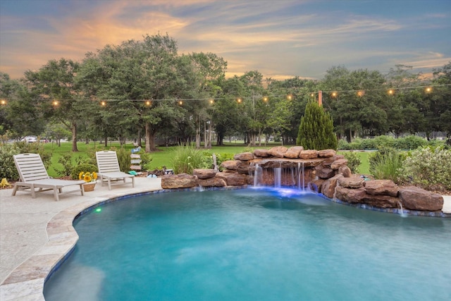 pool at dusk featuring a lawn, a patio, and an outdoor pool