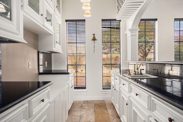 kitchen featuring dark countertops, a sink, white cabinetry, baseboards, and glass insert cabinets