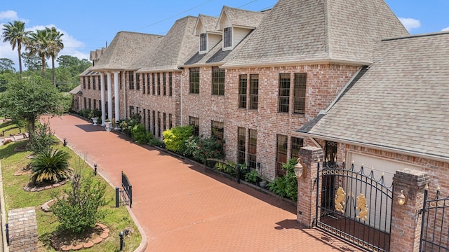 exterior space featuring brick siding, a shingled roof, fence, and a gate