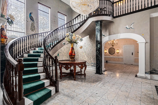 stairs with a towering ceiling, decorative columns, marble finish floor, and a notable chandelier