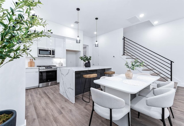3515 Mcilhenny St, Houston, TX 77004 - kitchen with modern cabinets, a kitchen bar, white cabinets, light wood finished floors, and appliances with stainless steel finishes