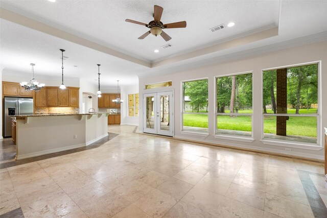 unfurnished living room featuring visible vents, crown molding, baseboards, a tray ceiling, and ceiling fan with notable chandelier