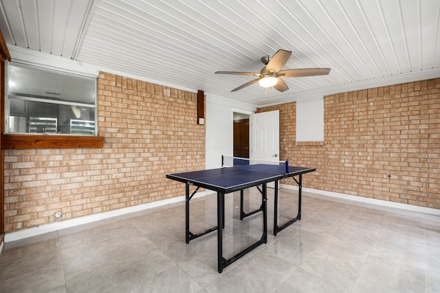 playroom featuring a ceiling fan, brick wall, baseboards, and wood ceiling