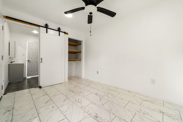unfurnished bedroom featuring a closet, marble finish floor, baseboards, ceiling fan, and a barn door