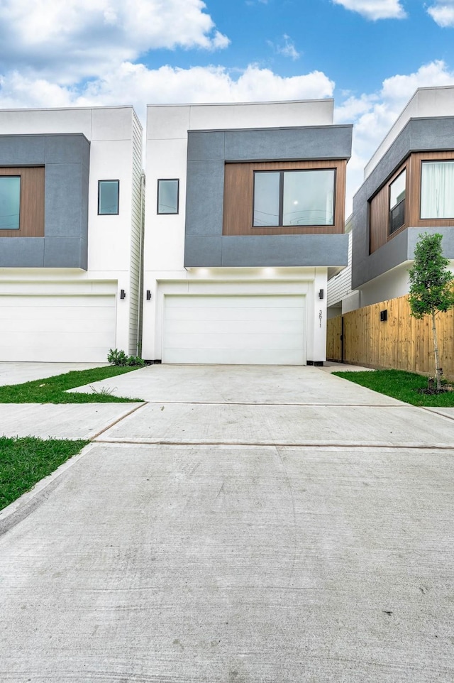 contemporary home with a garage, fence, stucco siding, and concrete driveway